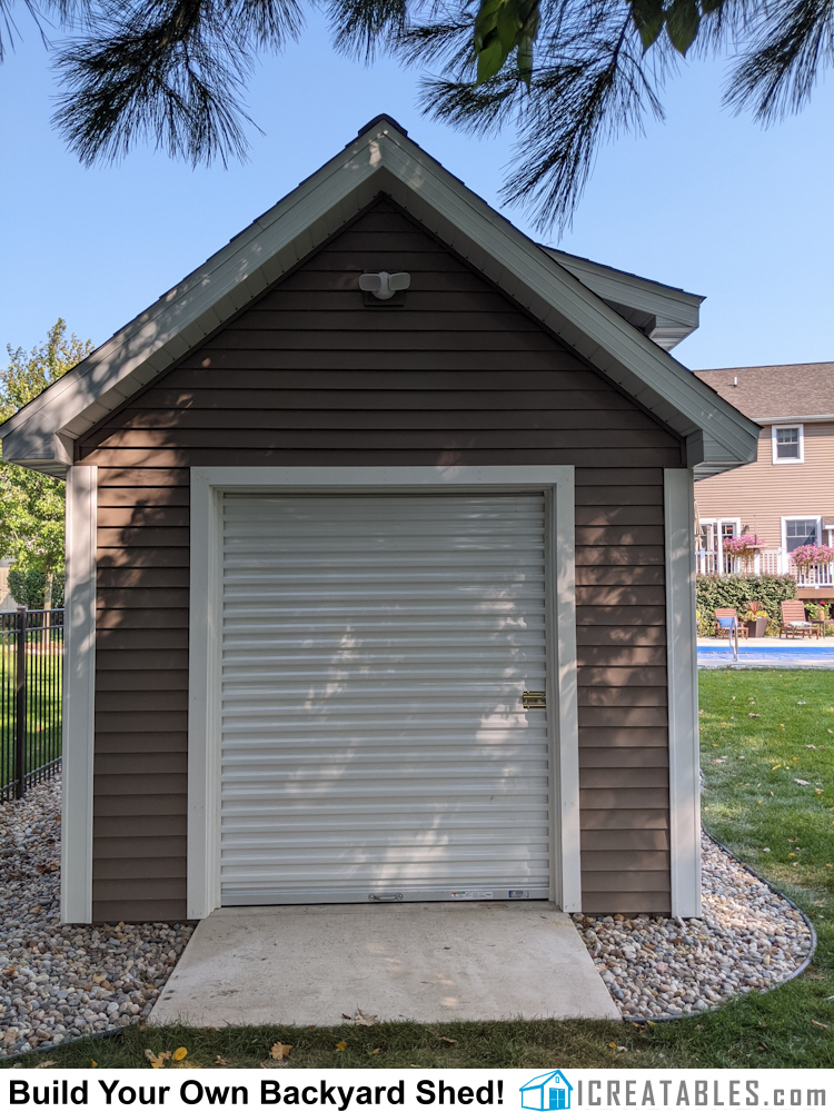 Overhead roll up garage door on backyard storage shed with dormer.